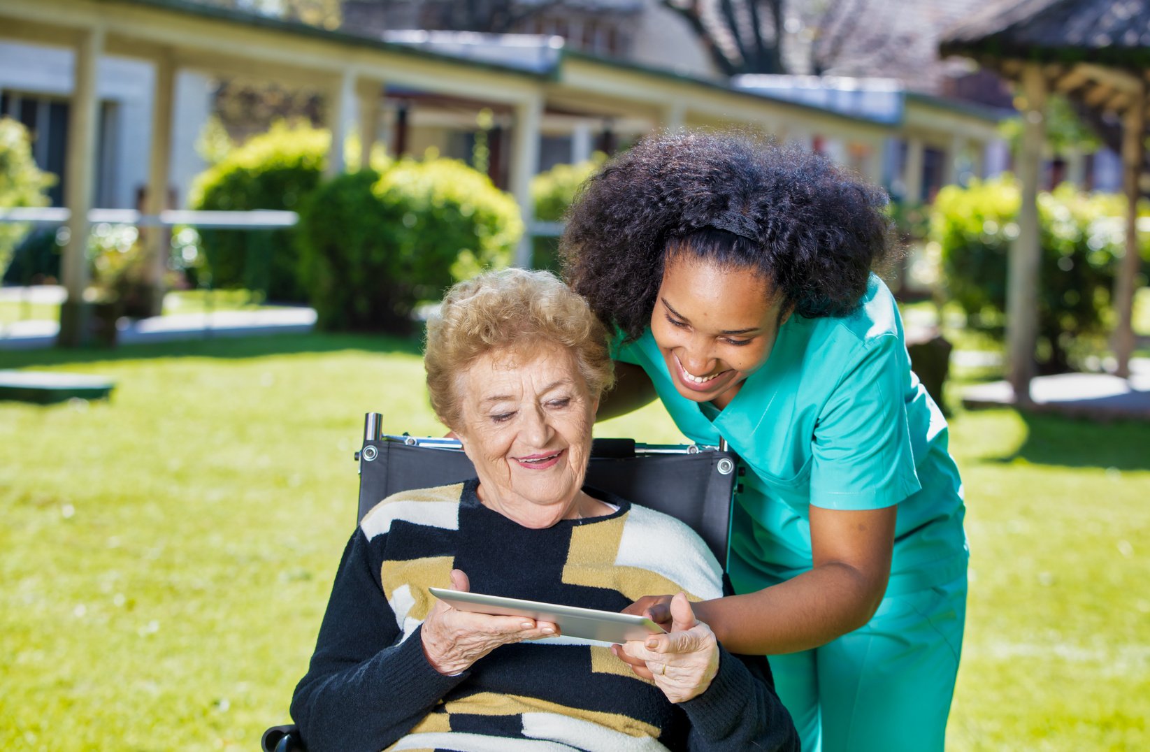 Caregivers at home. Disabled elderly lady showing photos of her grandchildren on tablet to caregiver